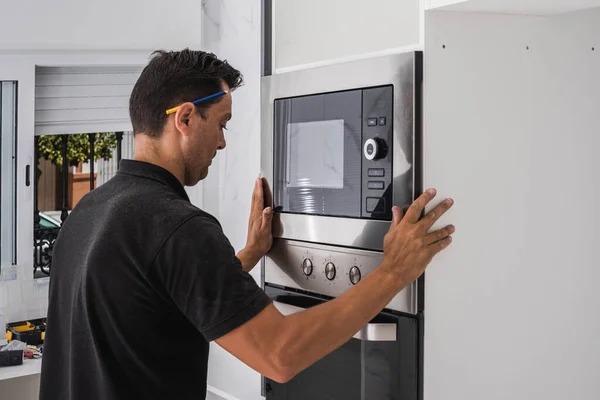 Man fitting a microwave inside the hole of a new kitchen cabinet — Stock Photo, Image