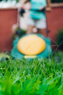 Odak noktasında çim biçme makinesi ve arka planda odaktan çıkmış bir kadın.