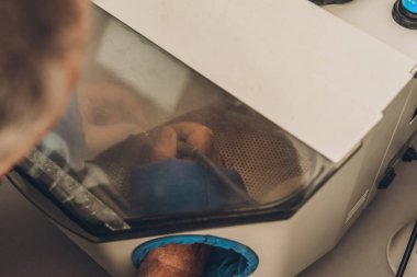 Kum püskürtme makinesinde çalışan bir adamın diş laboratuarındaki kalıpları parlatmak için yakın plan görüntüsü.