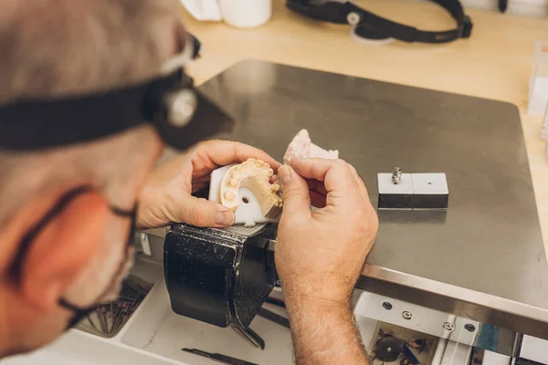 Vista de perto das mãos de um homem que trabalha em um dos pedaços de um molde de cerâmica em um laboratório odontológico — Fotografia de Stock