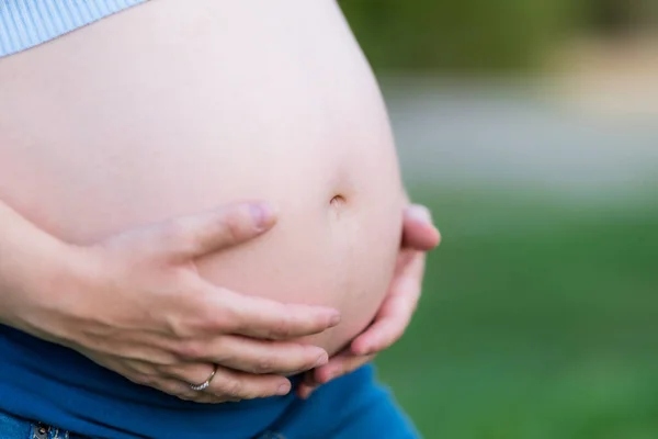 Närbild av händerna på en gravid kvinna som vidrör magen utomhus — Stockfoto