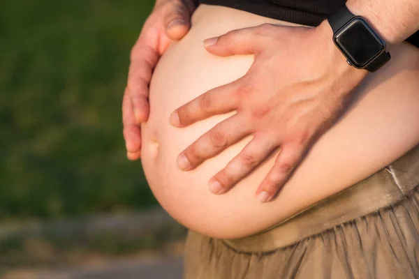 Close-up view of the hands of a man on the abdomen of a pregnant woman outdoors — Stock Photo, Image