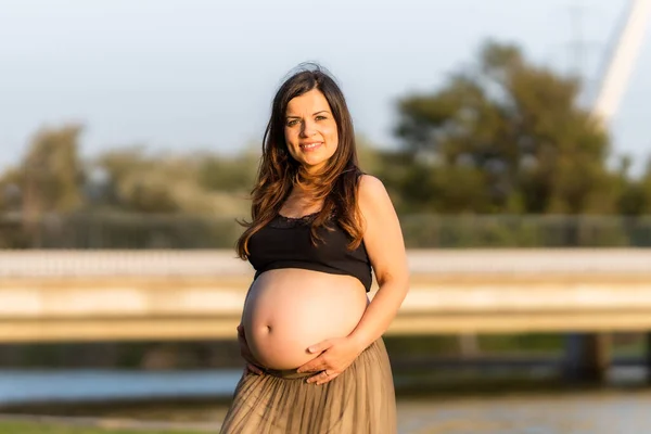Porträtt av en gravid kvinna som ler mot kameran stående i en urban sjö — Stockfoto