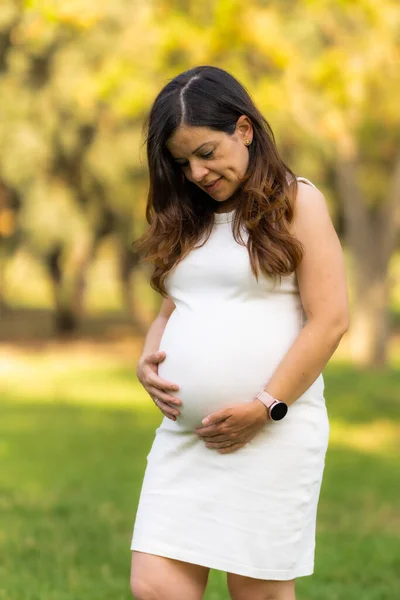 Foto vertical de una mujer de pie y mirando su vientre mientras lo toca —  Fotos de Stock