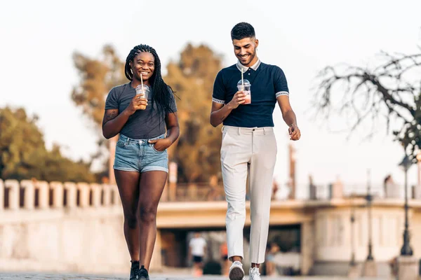 Two people of different ethnicities walking while drinking a shake outdoors