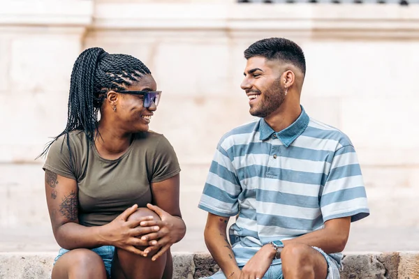 一个带着纹身和太阳镜的黑人女人坐在一个男人的旁边，在外面笑 — 图库照片
