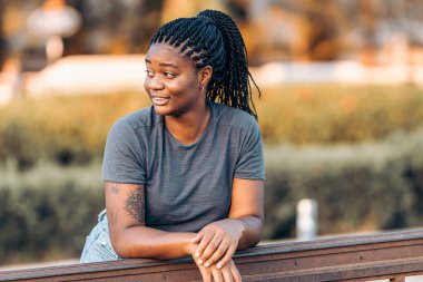 Sokakta korkuluklara yaslanmış yaz kıyafetleriyle dikkati dağılmış afro bir kadın.