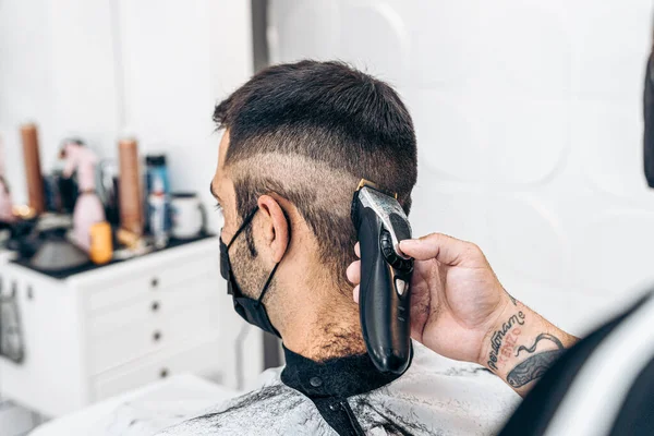 Barbeiro barbeando as costas da nuca de um homem com uma máscara em uma barbearia — Fotografia de Stock
