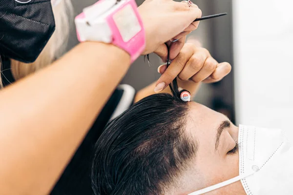 Saç kıvırmak için maske takan bir müşterinin saçına bigudi uygulayan kuaför. — Stok fotoğraf