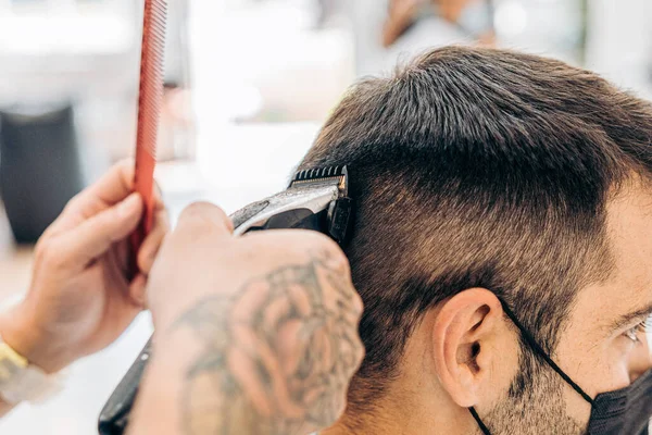 Vista de perto de um barbeiro cortando o cabelo de um homem com uma máquina em um salão — Fotografia de Stock