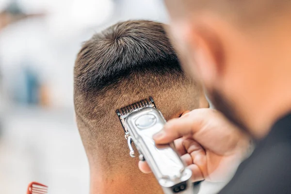 Barbeiro cortando o cabelo de um homem adulto com uma máquina de barbear — Fotografia de Stock