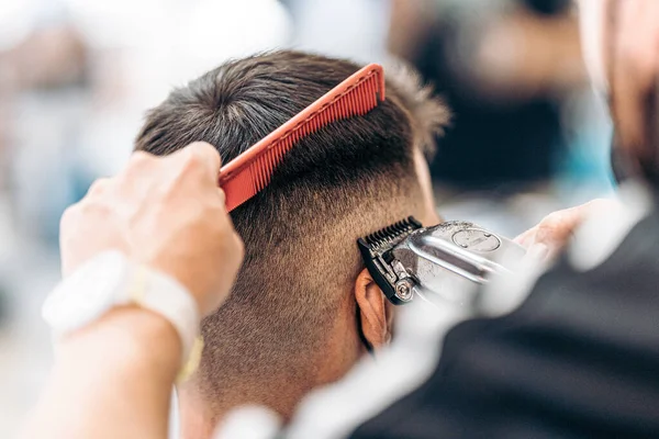 Barbeiro cortando o cabelo de um homem adulto com uma máquina de barbear e pente ca — Fotografia de Stock