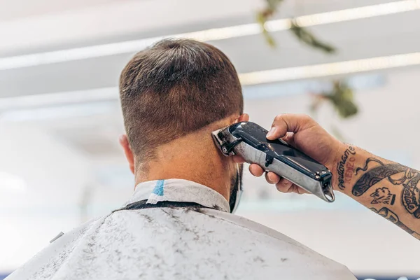 Mão de um barbeiro cortando o cabelo de um homem usando uma máquina elétrica — Fotografia de Stock