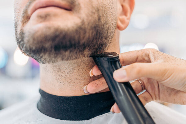 Обрезанная фотография руки парикмахера, бреющего мужчину в салоне