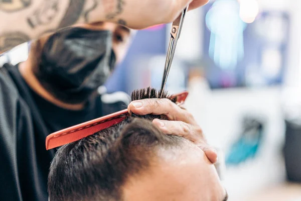 Barbeiro com máscara cortando o cabelo de um cliente em uma barbearia — Fotografia de Stock
