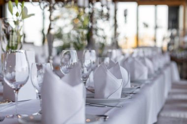 Çok güzel düzenlenmiş bir yemek masasında pürüzsüz beyaz örtüler, düzgün katlanmış peçeteler ve ışıl ışıl cam eşyalar var. Doğal ışık büyük pencerelerden içeri akarak atmosferi güçlendiriyor..