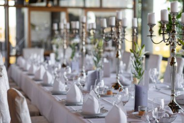 Uzun bir masa zarif şamdanlar, beyaz masa örtüleri ve düzgünce katlanmış peçetelerin yer aldığı özel bir durum için güzelce düzenlenmiştir. Hava sıcak ve davetkar..