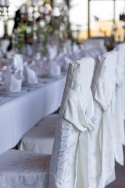 Zarif örtüleri ve dekoratif sofra takımlarıyla beyaz sandalyeler sergilenen özel bir etkinlik için uzun bir masa hazırlandı. Yumuşak ışık mekanı doldurur ve sıcak bir atmosfer yaratır..