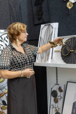 Bir sanat fuarında, bir kadın karmaşık bir şekilde tasarlanmış duvar sanat eserlerini inceliyor. Etrafı çeşitli dekoratif eşyalarla çevriliyken modern bir saate odaklanmış..