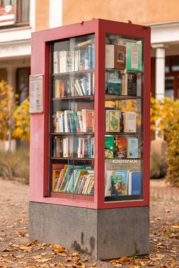 Sonbahar yapraklarıyla çevrili bir parkta renkli bir kitap değişim kutusu duruyor. Toplum okuryazarlığını desteklemek ve paylaşmak için çeşitli kitaplarla doludur..