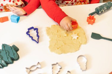 İki çocuk evde tatil pişirme etkinliğine katılmış renkli kurabiye kesiciler kullanarak hamurdan şekiller kesiyorlar. Sahne neşeli, şenlikli heyecanla dolu..