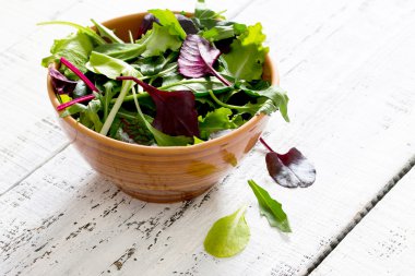 Beyaz ahşap bir masa üzerinde bir kapta taze yeşil karışık salata