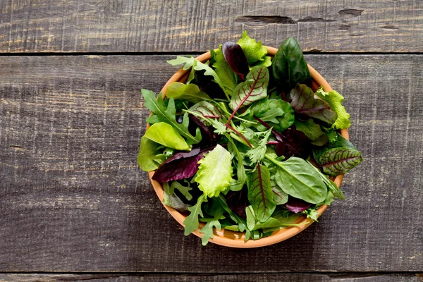 Salada mista verde fresca em uma tigela em uma mesa de madeira escura — Fotografia de Stock