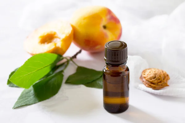 Minyak kosmetik dari biji persik dalam botol kaca pada abu-abu — Stok Foto