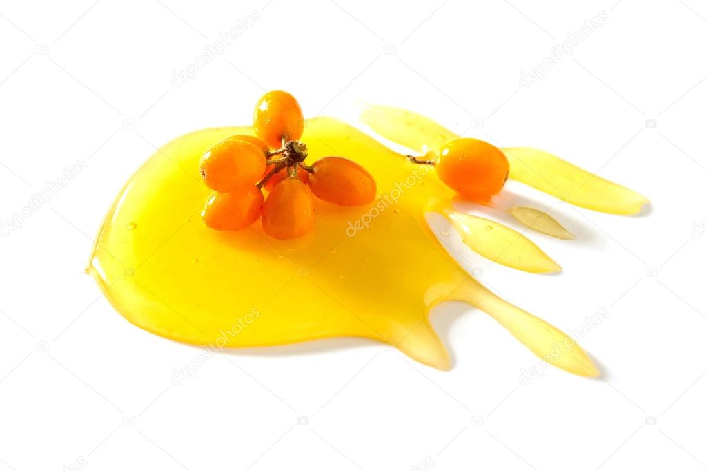 A drop of honey (maple syrup) and sea buckthorn berries on a whi