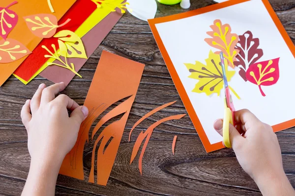Autumn leaves of colored paper on a wooden background. The child