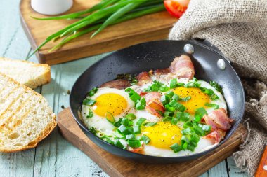 Baharda çırpılmış yumurta, yeşil soğan ve domuz pastırması. Kırsal ahşap arka planda dökme demir tavada..