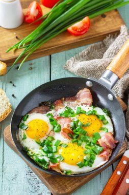 Baharda çırpılmış yumurta, yeşil soğan ve domuz pastırması. Kırsal ahşap arka planda dökme demir tavada..