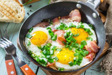 Baharda çırpılmış yumurta, yeşil soğan ve domuz pastırması. Kırsal ahşap arka planda dökme demir tavada..