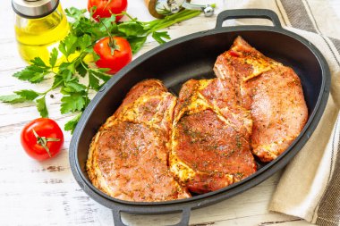 Kemiğin üzerinde taze çiğ domuz filetosu, baharatlar ve ahşap masadaki dökme demir tavada marine edilmiş terbiye, pişirme hazırlığı..