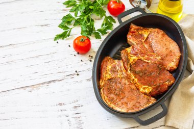 Kemiğin üzerine taze çiğ domuz filetosu, baharatlar ve ahşap masadaki dökme demir tavada marine edilmiş terbiye, pişirme hazırlığı. Boşluğu kopyala.