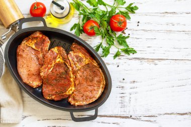 Kemiğin üzerine taze çiğ domuz filetosu, baharatlar ve ahşap masadaki dökme demir tavada marine edilmiş terbiye, pişirme hazırlığı. En üstteki düz yerde. Boşluğu kopyala.