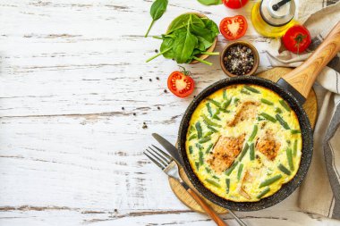 Sağlıklı kahvaltı ya da diyet öğle yemeği. Köy omleti (omlet, omlet), somon fileto ve yeşil fasulye ile birlikte beyaz bir mutfak ahşap masasında tavada. En üstteki düz yerde. Boşluğu kopyala.