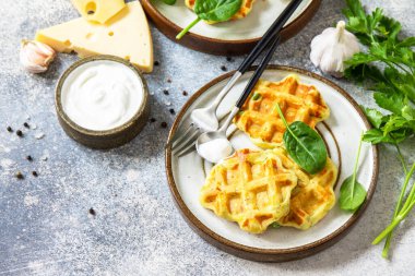 Potato waffles with peas, paprika, cheese and herbs, a quick snack in a plate on a gray stone countertop. Copy space.