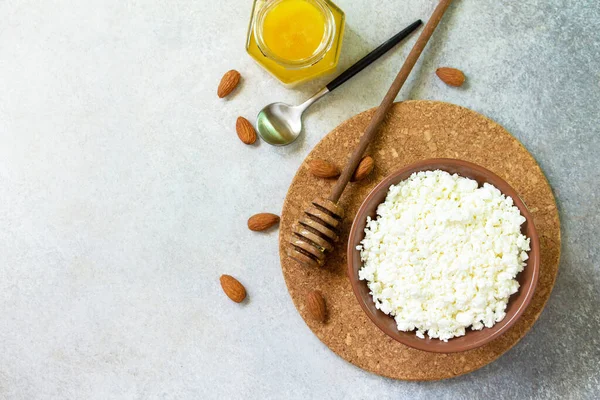 Rich in calcium healthy food. Tvorog, farmers cheese, curd cheese or cottage cheese in a bowl with honey and almond on stone table. Top view flat lay. Copy space.