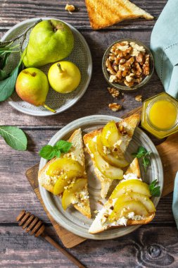 Sağlıklı yaz kahvaltısı ya da aperatif, antipasto. Ahşap bir masada karamelli armut, bal, fındık ve peynirli ricotta ile ızgara tost. Üst görünüm düzlüğü.