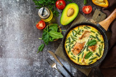 Kahvaltı ya da öğle yemeği konsepti. Köy usulü omlet (omlet, omlet), somon filetosu ve yeşil fasulye ile birlikte taştan bir arka planda kızartma tavasında. Üst manzara, düz yatış. Boşluğu kopyala.