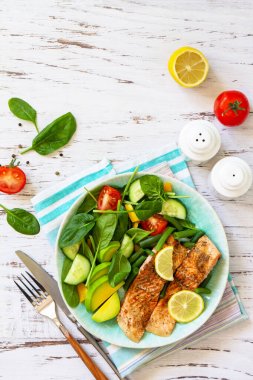 Grilled salmon fillet with spinach, cucumber, tomato and avocado salad on a white wooden table. Top view, flat lay. Copy space. clipart