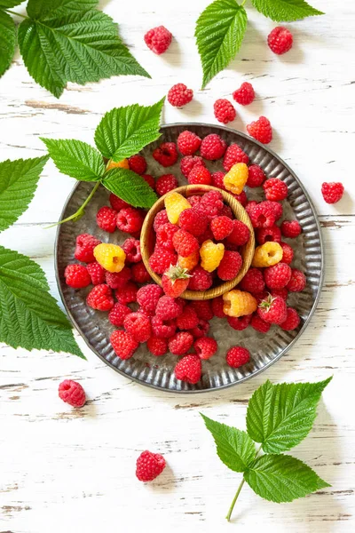 Ripe juicy sweet berries of yellow and red raspberries on a white rustic table. Top view flat lay background.