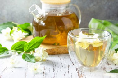 Terapötik bitki çayı. Yasemin çiçekli sıcak yasemin çayı kırsal bir ahşap masada cam çaydanlıkta.. 