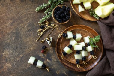 Meyve ve böğürtlenli kanepelerin ziyafeti. Cadılar Bayramı partisi yemeği. Ahşap bir masada kavunlu ve böğürtlenli kanepeler. Üst görünüm düz arkaplan. Boşluğu kopyala.