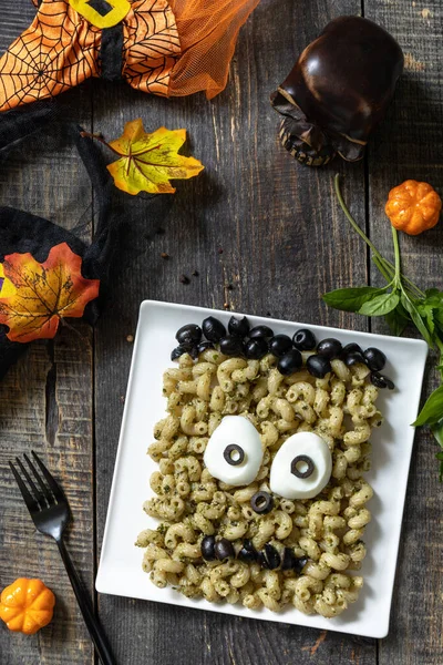 Halloween funny idea for party food, decoration celebration kid party meal. Halloween with pesto creative Pasta shaped Frankenstein monster. Top view flat lay background.