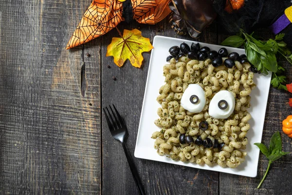 Halloween funny idea for party food, decoration celebration kid party meal. Halloween with pesto creative Pasta shaped Frankenstein monster. Top view flat lay background. Copy space.