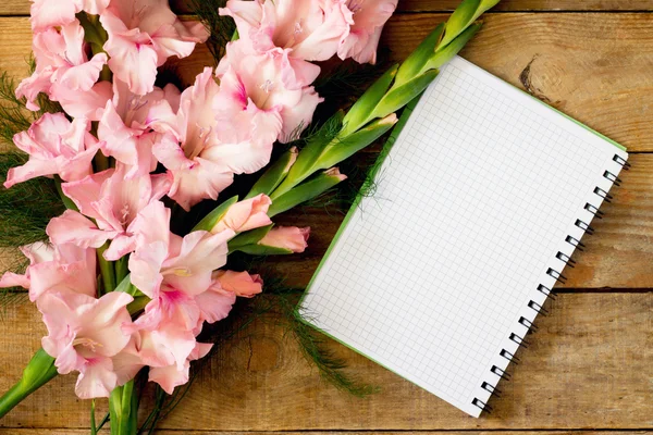 Kwiaty różowe gladioluses i notebook — Zdjęcie stockowe