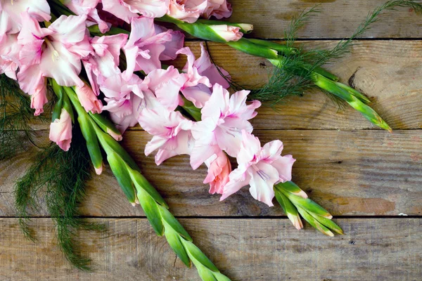 Розовые гладиолусы на деревянном столе — стоковое фото
