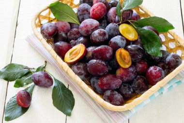 Beyaz ahşap bir masa üzerinde bir hasır sepet içinde Erik